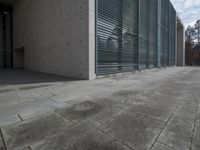 a concrete building with some windows next to some brick paving and stone ground with a bench in front