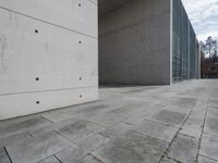 a concrete building with some windows next to some brick paving and stone ground with a bench in front