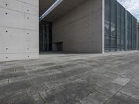 a concrete building with some windows next to some brick paving and stone ground with a bench in front