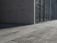 a concrete building with some windows next to some brick paving and stone ground with a bench in front