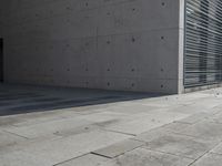 a concrete building with some windows next to some brick paving and stone ground with a bench in front