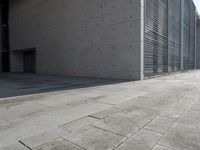 a concrete building with some windows next to some brick paving and stone ground with a bench in front