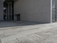 a concrete building with some windows next to some brick paving and stone ground with a bench in front