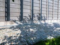 a brick sidewalk with a planter and windows in front of it and shadow on the street