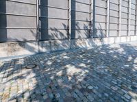 a brick sidewalk with a planter and windows in front of it and shadow on the street