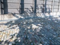 a brick sidewalk with a planter and windows in front of it and shadow on the street