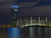 a boat sailing along a calm river by a tall building with a sky display in the background