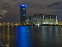 a boat sailing along a calm river by a tall building with a sky display in the background