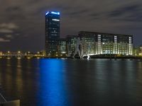 a boat sailing along a calm river by a tall building with a sky display in the background