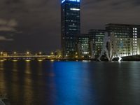 a boat sailing along a calm river by a tall building with a sky display in the background