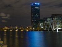 a boat sailing along a calm river by a tall building with a sky display in the background