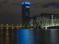 a boat sailing along a calm river by a tall building with a sky display in the background