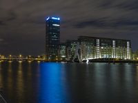 a boat sailing along a calm river by a tall building with a sky display in the background