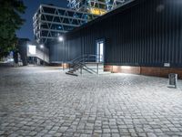 a black building sits across from another building with some stairs to it and is at night