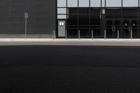 a black building has many glass windows and is empty, with a single stop sign