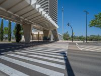 a car sitting at an empty street underneath a overpass overhang that contains a train stop, and cars and a pedestrian