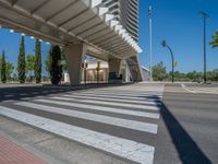 a car sitting at an empty street underneath a overpass overhang that contains a train stop, and cars and a pedestrian