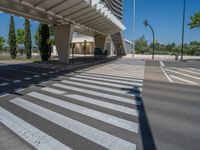 a car sitting at an empty street underneath a overpass overhang that contains a train stop, and cars and a pedestrian