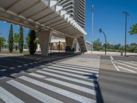 a car sitting at an empty street underneath a overpass overhang that contains a train stop, and cars and a pedestrian