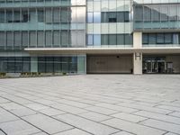 a large gray building with a small courtyard in front of it has a sky background