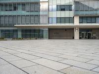 a large gray building with a small courtyard in front of it has a sky background