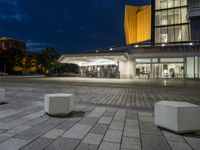 an empty plaza and a lit up building at night with two square stone benches in front