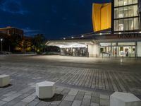 an empty plaza and a lit up building at night with two square stone benches in front