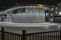 the bus is passing past a modern building in the city street at night time,