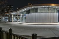 the bus is passing past a modern building in the city street at night time,