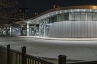 the bus is passing past a modern building in the city street at night time,