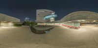 an outdoor seating area at night in front of a modern building with curved columns and concrete roof