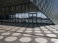 people are walking around in the courtyard of a modern building with circular glass walls, a parking lot, and several cars