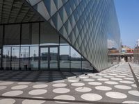 people are walking around in the courtyard of a modern building with circular glass walls, a parking lot, and several cars