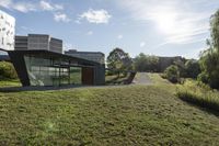 the sun is shining on a modern building, with green grass and plants, near a river