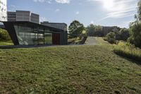 the sun is shining on a modern building, with green grass and plants, near a river