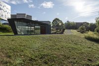 the sun is shining on a modern building, with green grass and plants, near a river