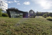 the sun is shining on a modern building, with green grass and plants, near a river