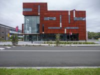 a red modern building surrounded by greenery in front of it is a bike rack that is standing at the corner