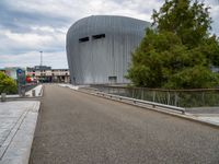 a view of the modern building that has a curved roof and gated in area with trees