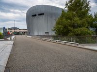 a view of the modern building that has a curved roof and gated in area with trees