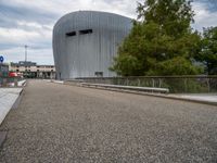 a view of the modern building that has a curved roof and gated in area with trees