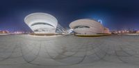 a view of a large white building with circular shapes and light up at night and in the background