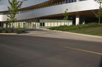 this is a modern building with glass and wood accents and glass walls, along the street, a lawn and a tree
