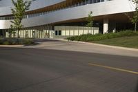 this is a modern building with glass and wood accents and glass walls, along the street, a lawn and a tree