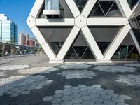 the modern building is constructed into hexagons on a sidewalk of brick stones