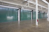 an empty large indoor storage facility with no floor space to work on it and two green rolling up doors