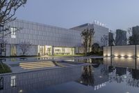 a modern white building is lit up with lights on and reflecting in a pool of water