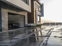 a long driveway with a few cars and a bike parked under a building in the rain