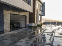 a long driveway with a few cars and a bike parked under a building in the rain