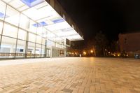 a large glass building on a bricked floor in front of a parking lot at night